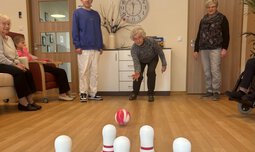 Senioren beim Kegeln in einem Zimmer mit einem Betreuer | © Caritas München und Oberbayern