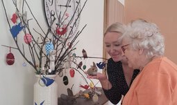Eine Betreuerin und eine Seniorin betrachten einen gebastelten Osterzweigbusch mit Dekorierung | © Caritas München und Oberbayern